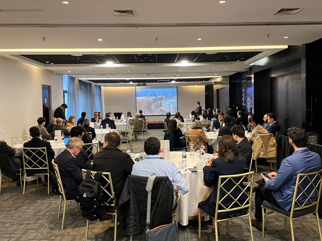 Presentación al plenario con el expositor y las diapositivas al fondo, y mesas de trabajo ya dispuestas en el salón